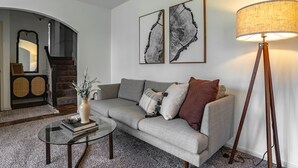 A living room with a grey sofa, a round coffee table, a floor lamp, and two framed abstract artworks on the wall.