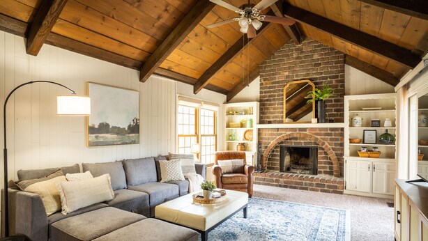 A cozy living room with a fireplace, wooden ceiling beams, a sofa, and a coffee table.