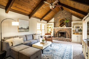 A cozy living room with a fireplace, wooden ceiling beams, a sofa, and a coffee table. - Secluded, updated 4BR, kid friendly, 5 min from restaurants (Overland Park)
