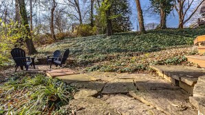 A stone pathway leading to a seating area with two Adirondack chairs and a small table.