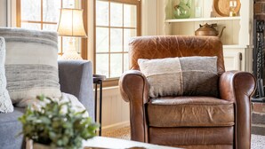A cozy living room with a brown leather armchair, a grey sofa, and a lamp.