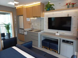 A compact living space with a kitchenette, a flat-screen TV mounted on a wall, a sofa, and a small dining table. - Studio/apartment (São Paulo)