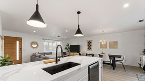 A modern kitchen with a large island, black pendant lights, and a dining area with a table and chairs. - Vista del Valle 🌵 Pickleball + Pitch&Putt + Hot Tub + Pool (Joshua Tree)