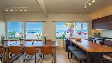A modern kitchen with a large island, wooden furniture, and large windows offering ocean views.