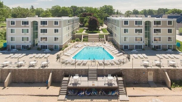 Un hotel moderno con piscina central, varios balcones y jardín ajardinado.