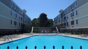 Una piscina rectangular rodeada por una cerca, con una escalera que lleva a un edificio al fondo.