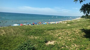 Una playa con gente nadando y tomando el sol, sombrillas y barcos en el agua.
