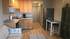 Una cocina compacta con armarios de madera, un refrigerador, una cafetera y una pequeña mesa de comedor.