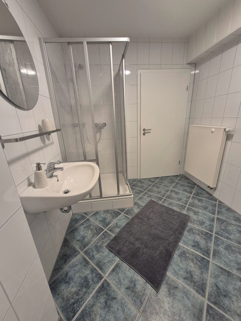 A bathroom with a shower, sink, and tiled floor.
