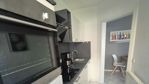 A modern kitchen with a built-in oven, a coffee maker, and a dining area with a chair and a table. - Funke Vacation Rental (Reichshof)