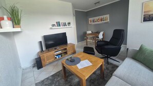 A modern living room with a flat-screen TV, wooden coffee table, black leather sofa, and a grey couch. - Funke Vacation Rental (Reichshof)