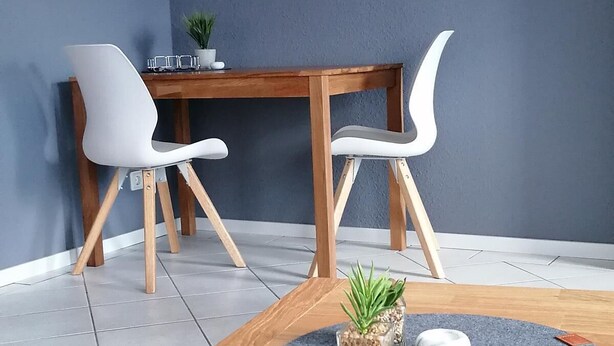 A modern dining area with a wooden table, two white chairs, a grey rug, and a potted plant. - Funke Vacation Rental (Reichshof)