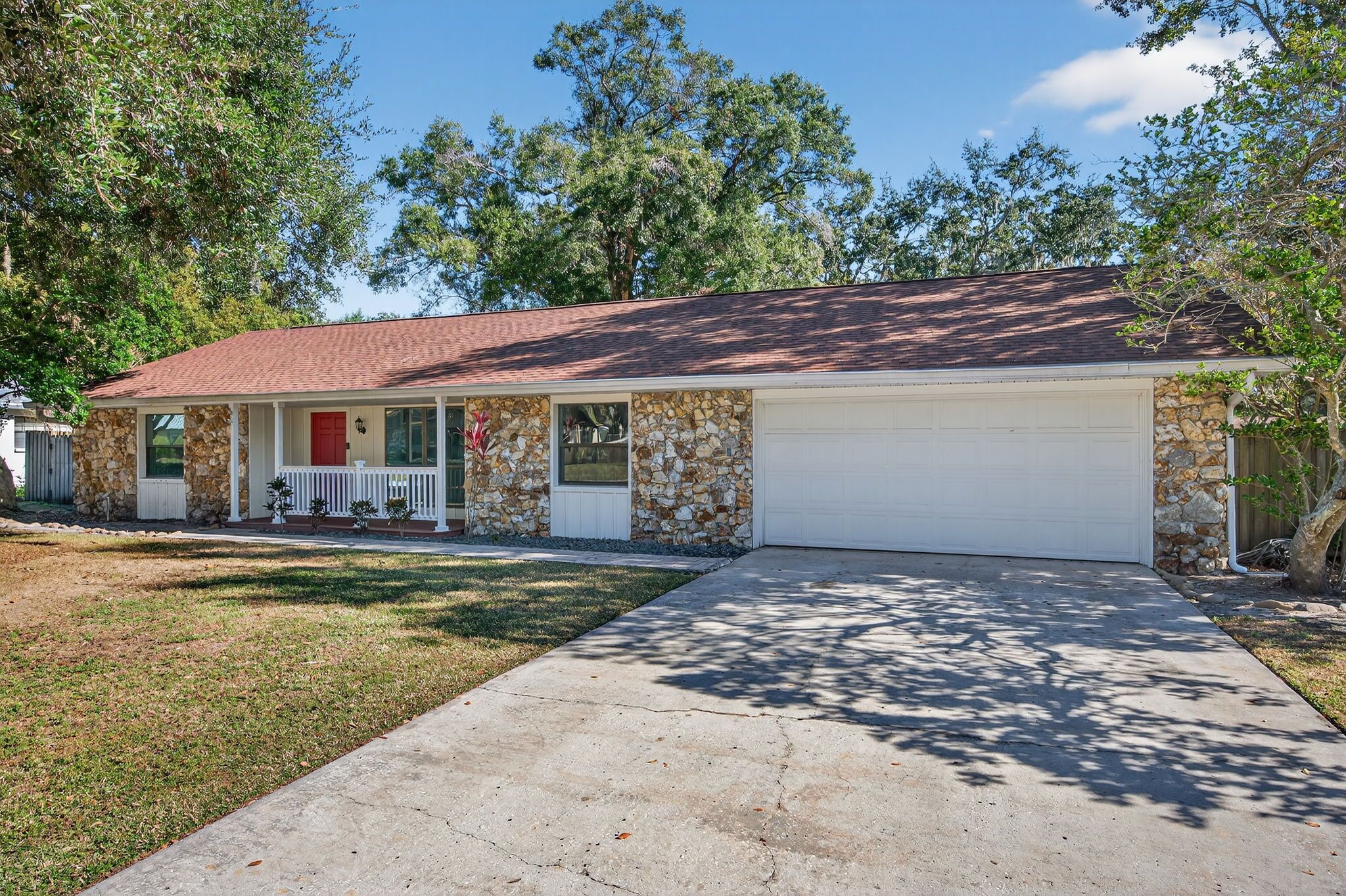 A single-story house with a stone facade, a red roof, and a white garage door.