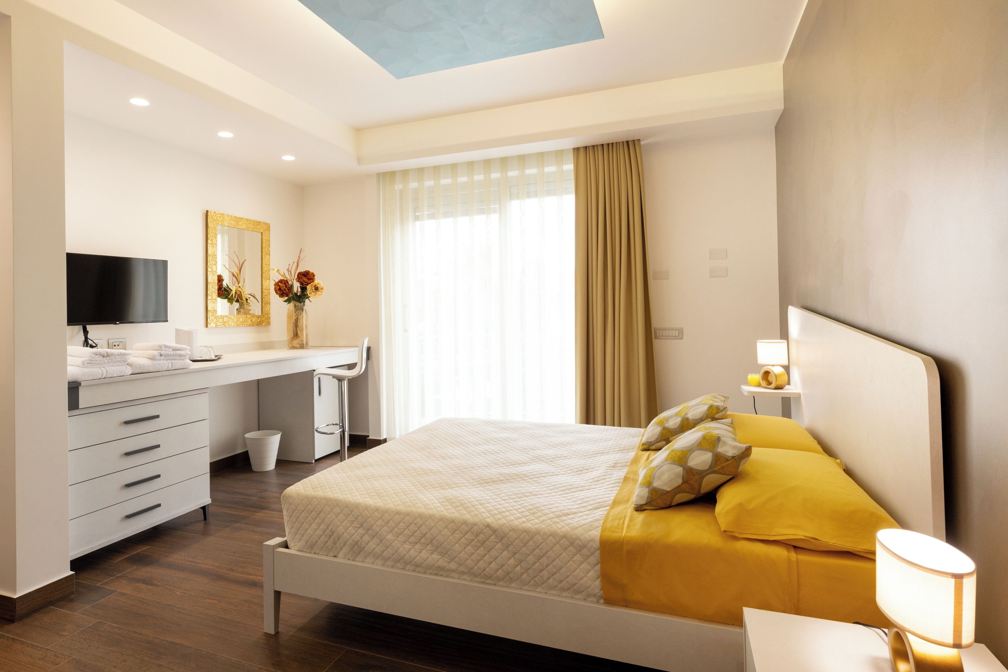 A modern hotel room with a bed, a desk, a TV, and a window with curtains.