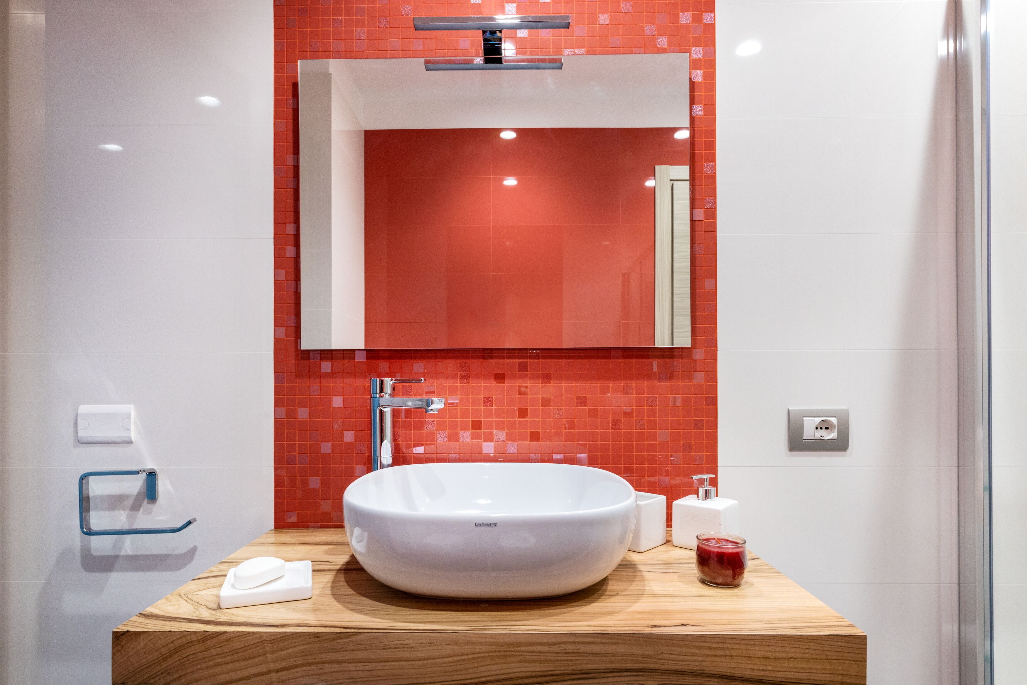 Une salle de bain moderne avec un lavabo rond blanc, un miroir au-dessus et un mur recouvert de carreaux rouges.