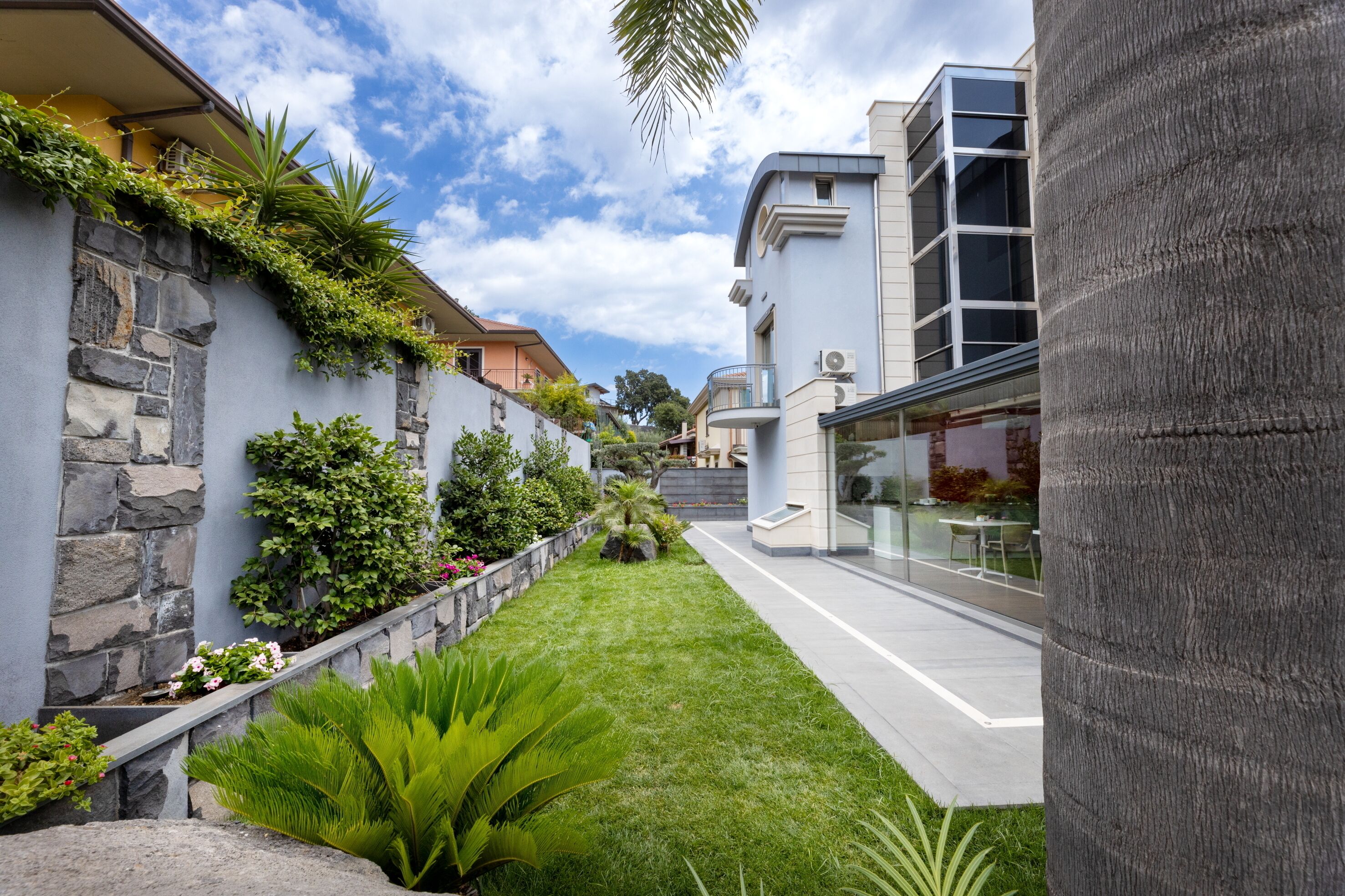 A modern building with a stone facade, a well-maintained garden, and a clear sky.