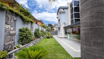 A modern building with a stone facade, a well-maintained garden, and a clear sky.