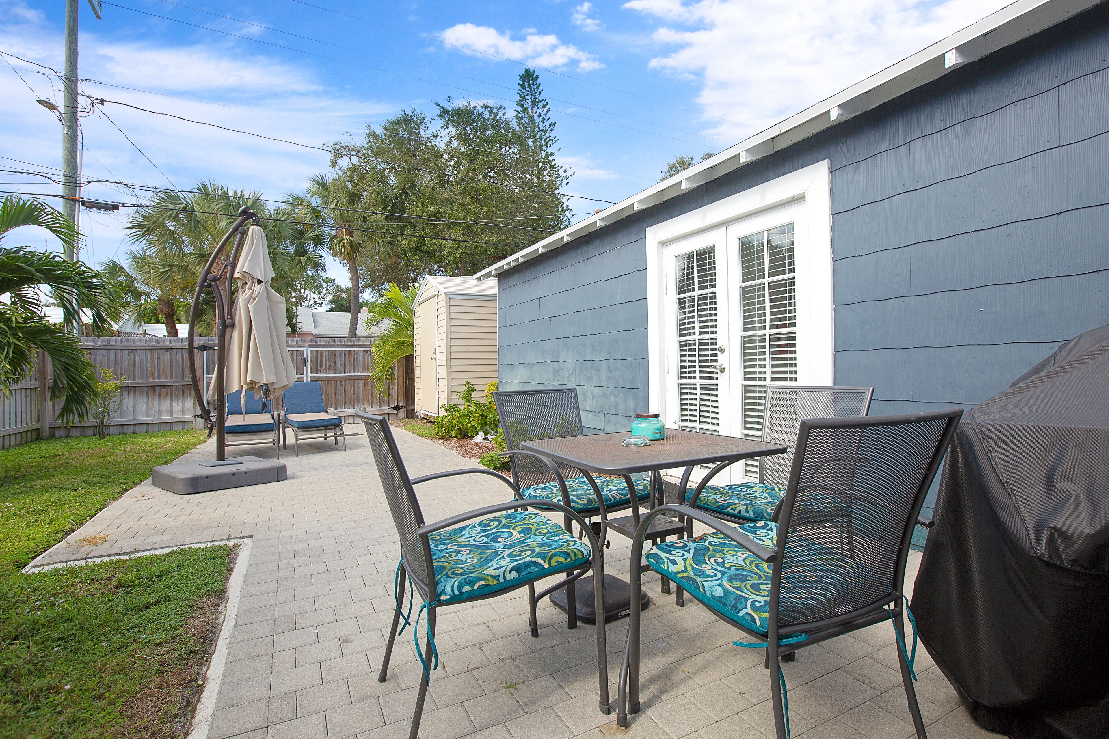 A patio with a table and chairs, a covered grill, and a small garden area.