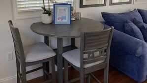 A dining area with a round table, four chairs, a blue couch, and framed artwork on the wall.
