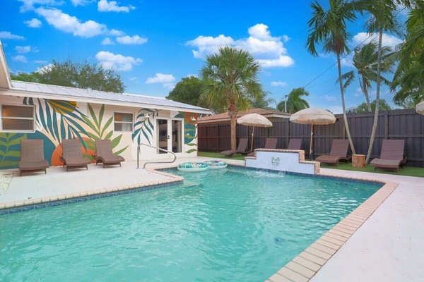 A backyard oasis w/ a large heated pool, lounge chairs, umbrellas, & waterfall.