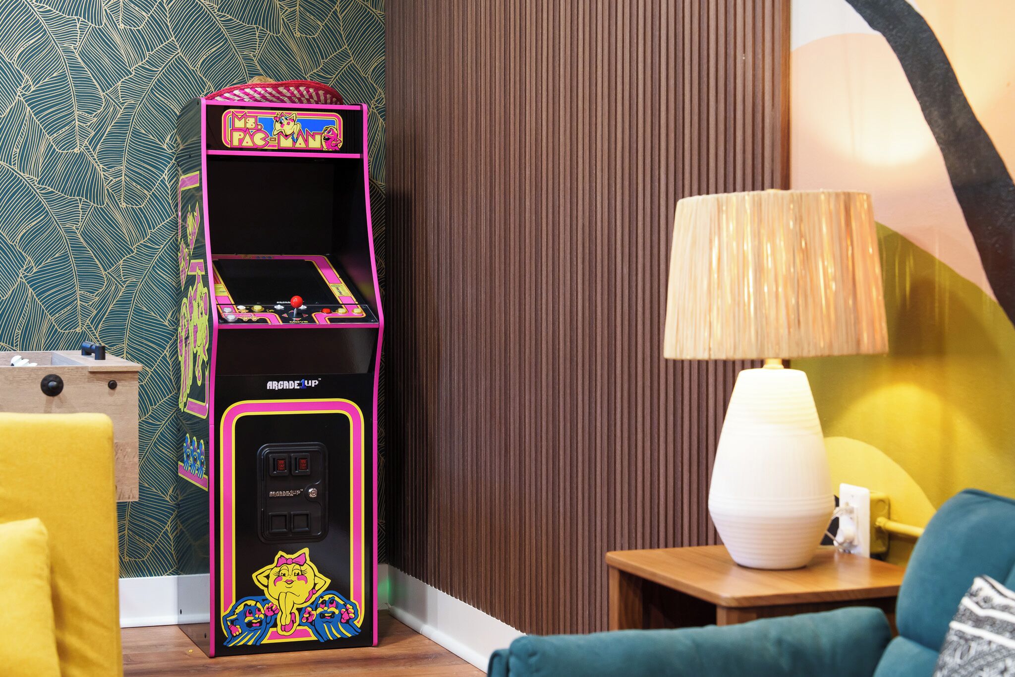 A room with a retro arcade machine, a lamp, and a sofa.