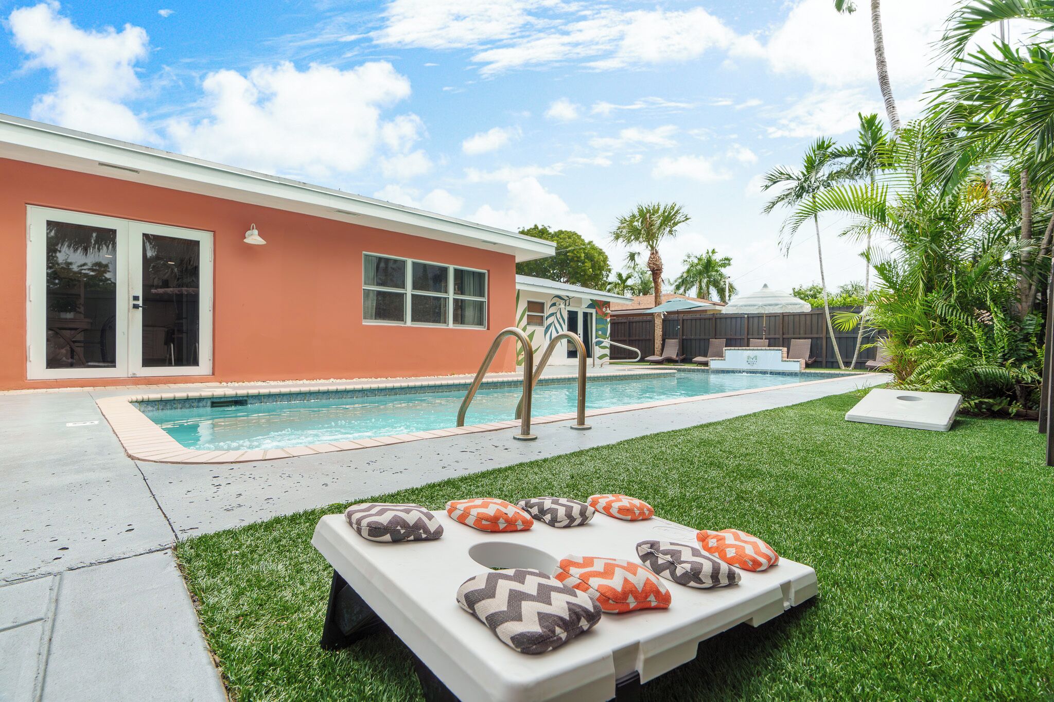A swimming pool with a slide, a lounge chair with pillows, and a house with a red exterior.