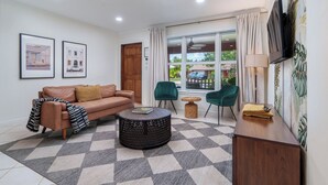 Un salón con sofá, sillones, una mesa de centro y un televisor montado en la pared.
