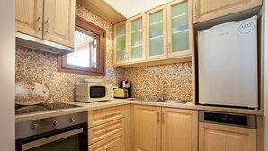 Een compacte keuken met houten kastjes, een inbouwoven, een magnetron, een koelkast en een vaatwasser.