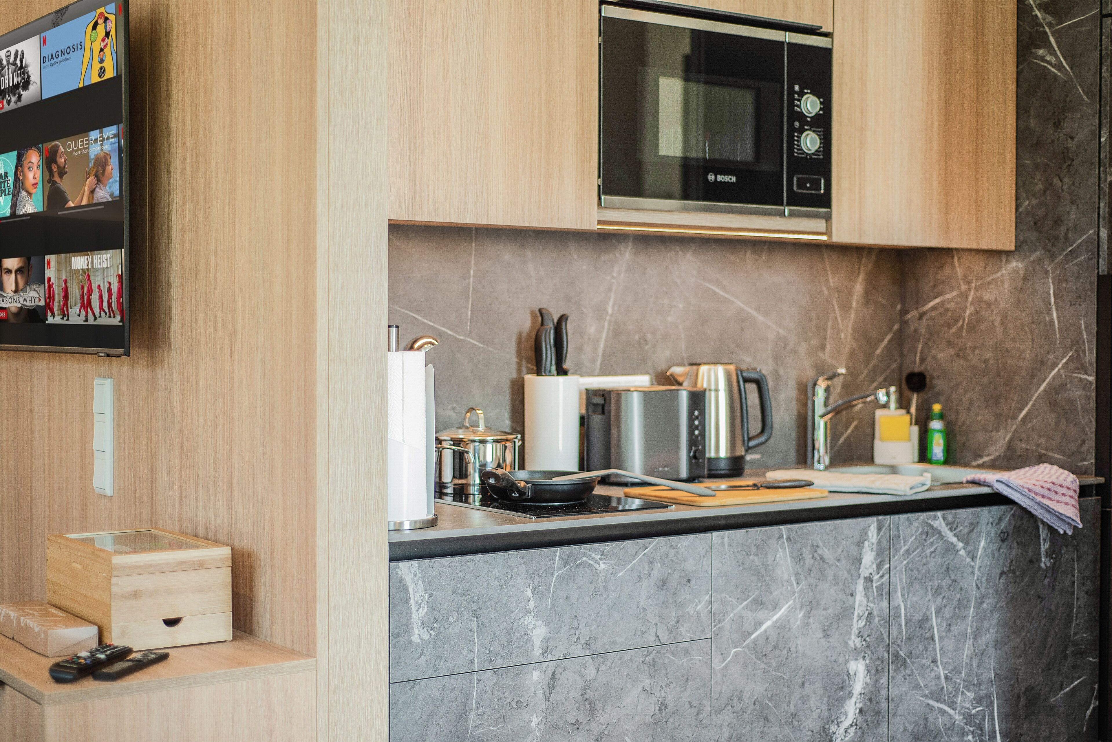 Een moderne keuken met een magnetron, fornuis en diverse apparaten. Er is een plank met boeken en een klein houten kastje.