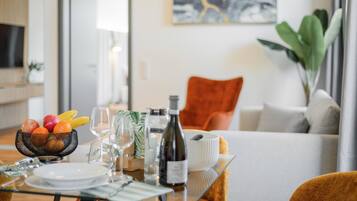 A dining table set with fruits, wine, and glasses, a sofa, and a plant in a modern living room.