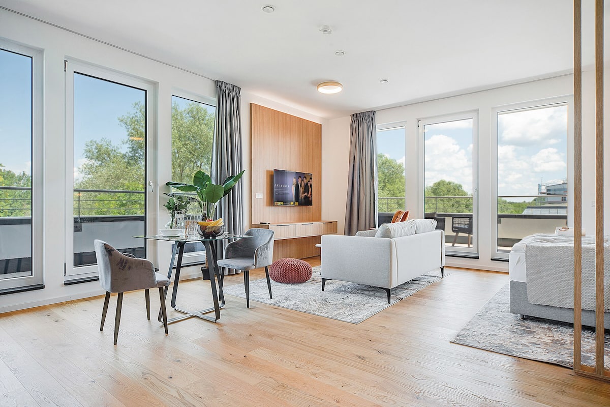 A spacious living area with a sofa, chairs, a dining table, and a TV.