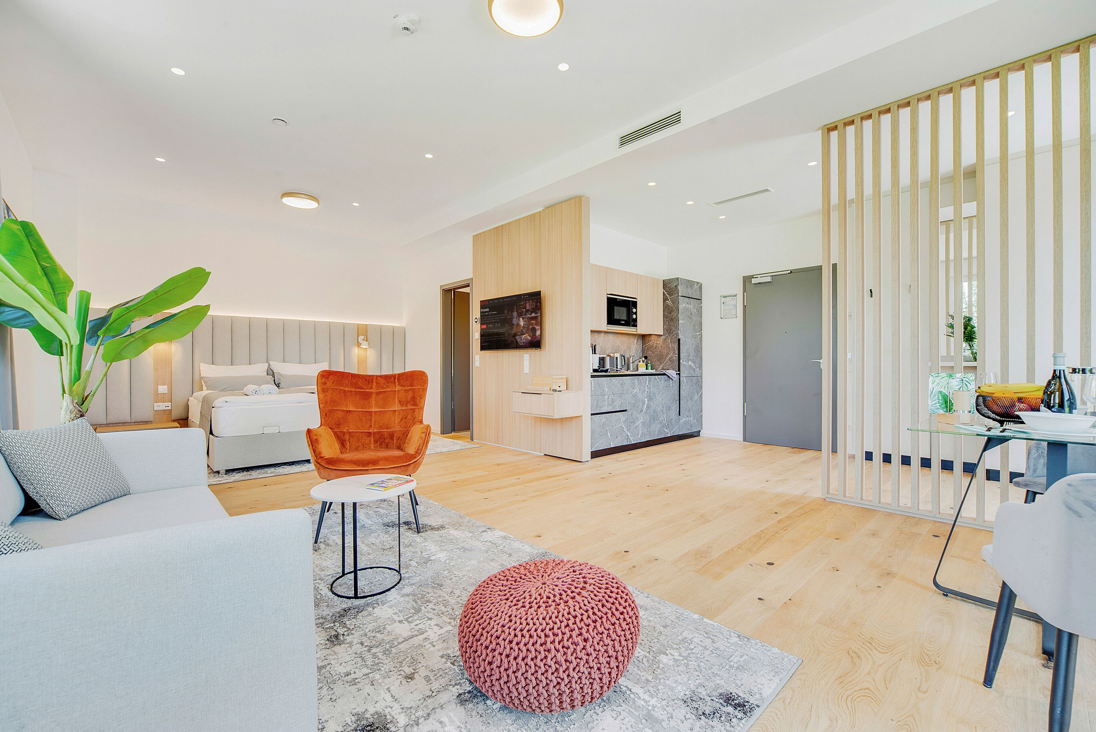 Un salon moderne avec un canapé, un pouf rouge en tricot et un plancher en bois.