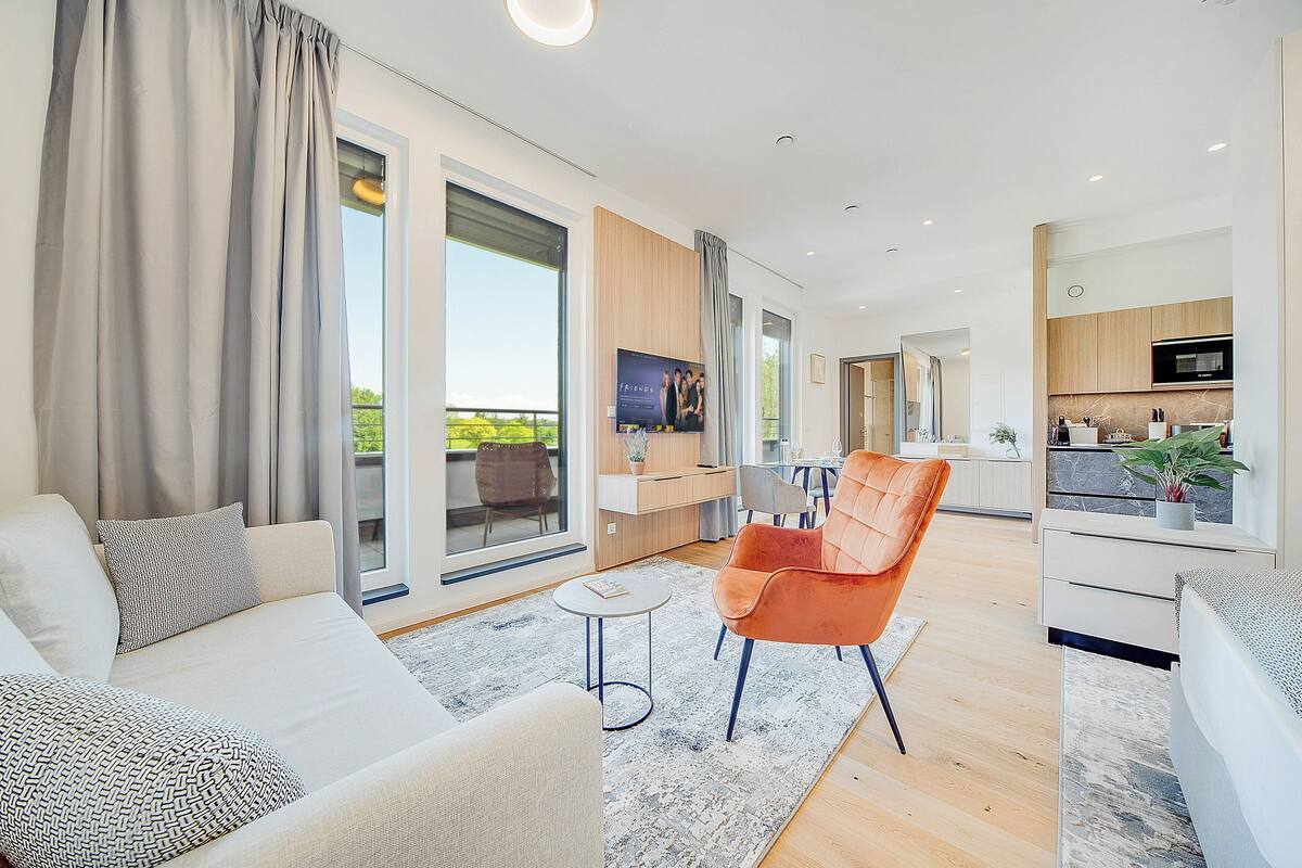 A modern living room with a sofa, armchair, and coffee table, connected to a kitchen area with a dining table and chairs.