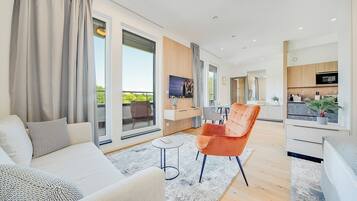 A modern living room with a sofa, armchair, and coffee table, connected to a kitchen area with a dining table and chairs.