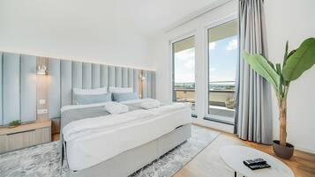 Un dormitorio moderno con una cama grande, una mesita, una planta en maceta y vistas al exterior.