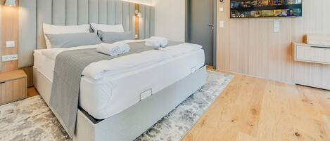 Un dormitorio moderno con una cama grande, un cabecero con iluminación integrada, un televisor de pantalla plana en la pared y piso de madera.