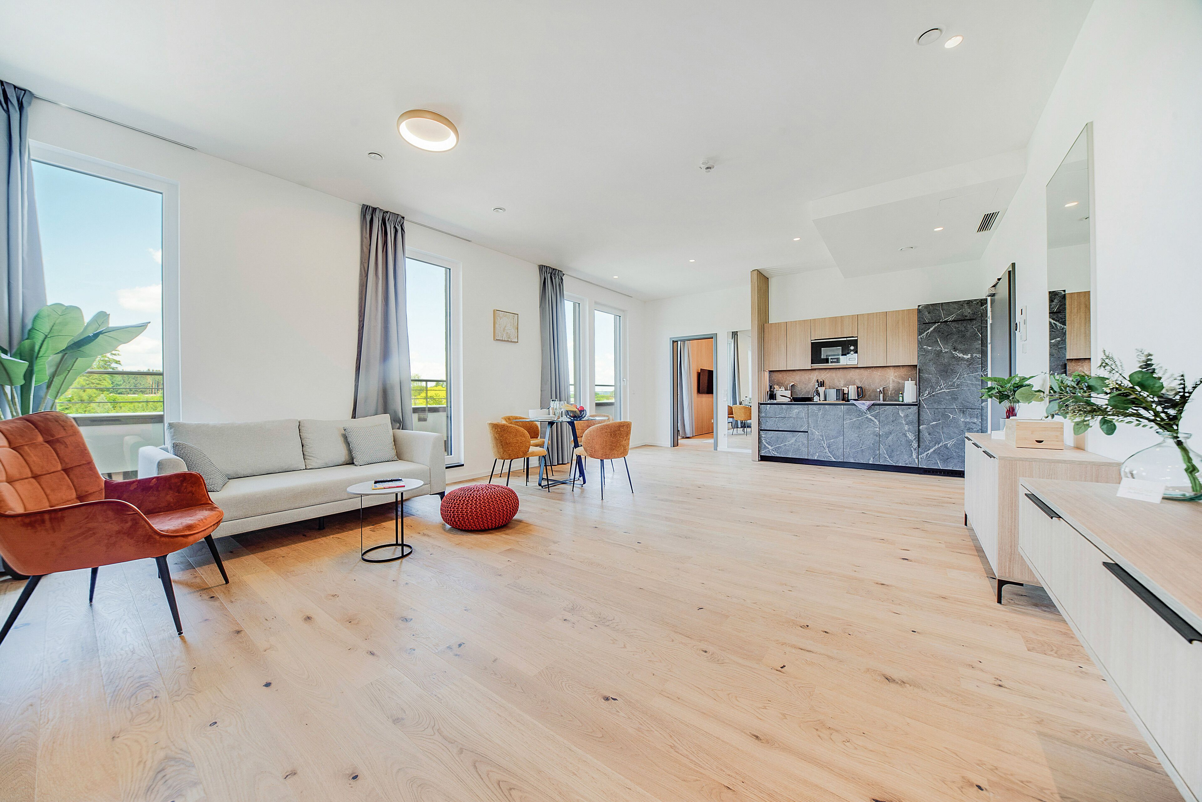 A spacious living area with a sofa, chairs, and a dining table. A kitchen is visible in the background with modern appliances.
