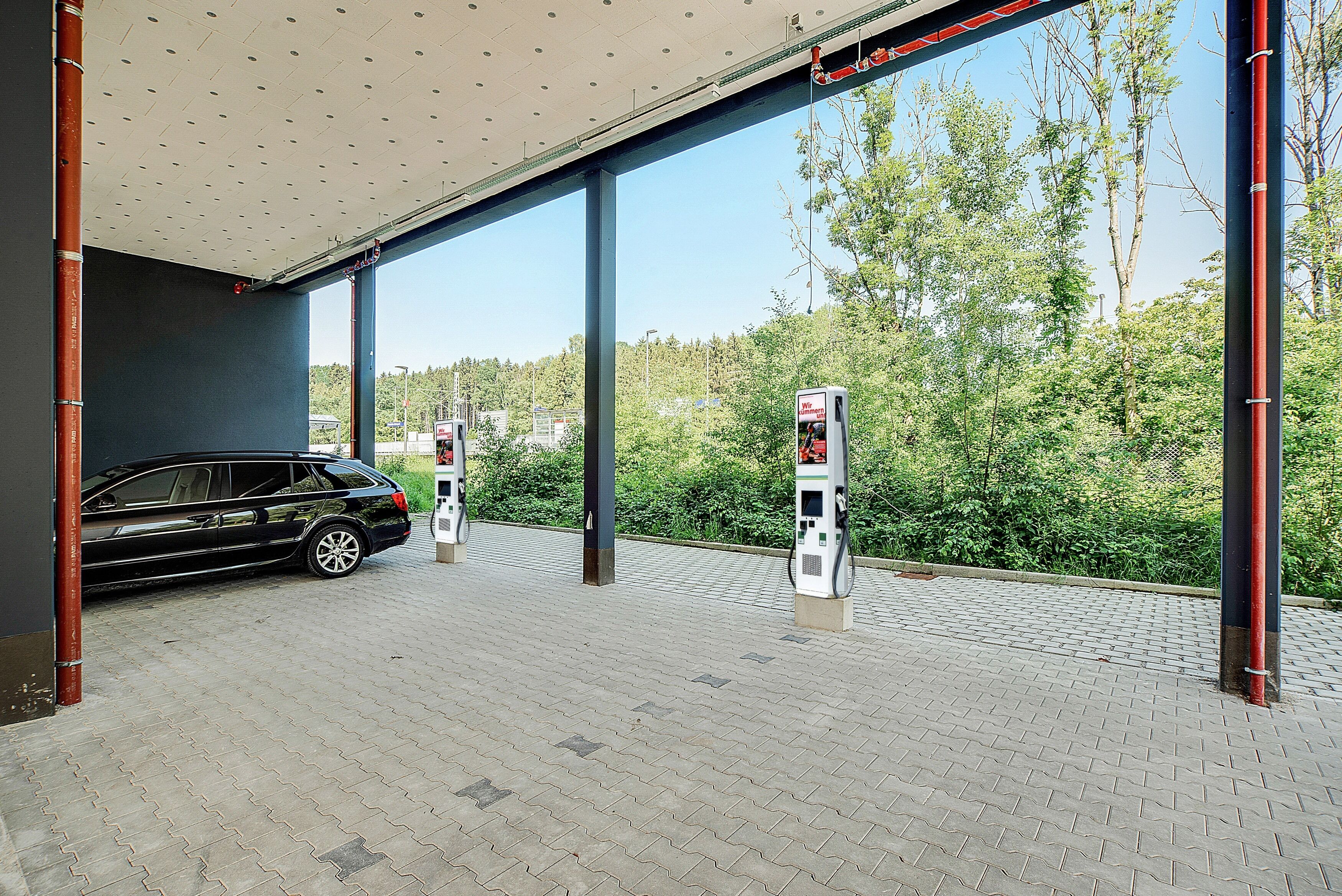 A covered parking area with a car and two fuel pumps.