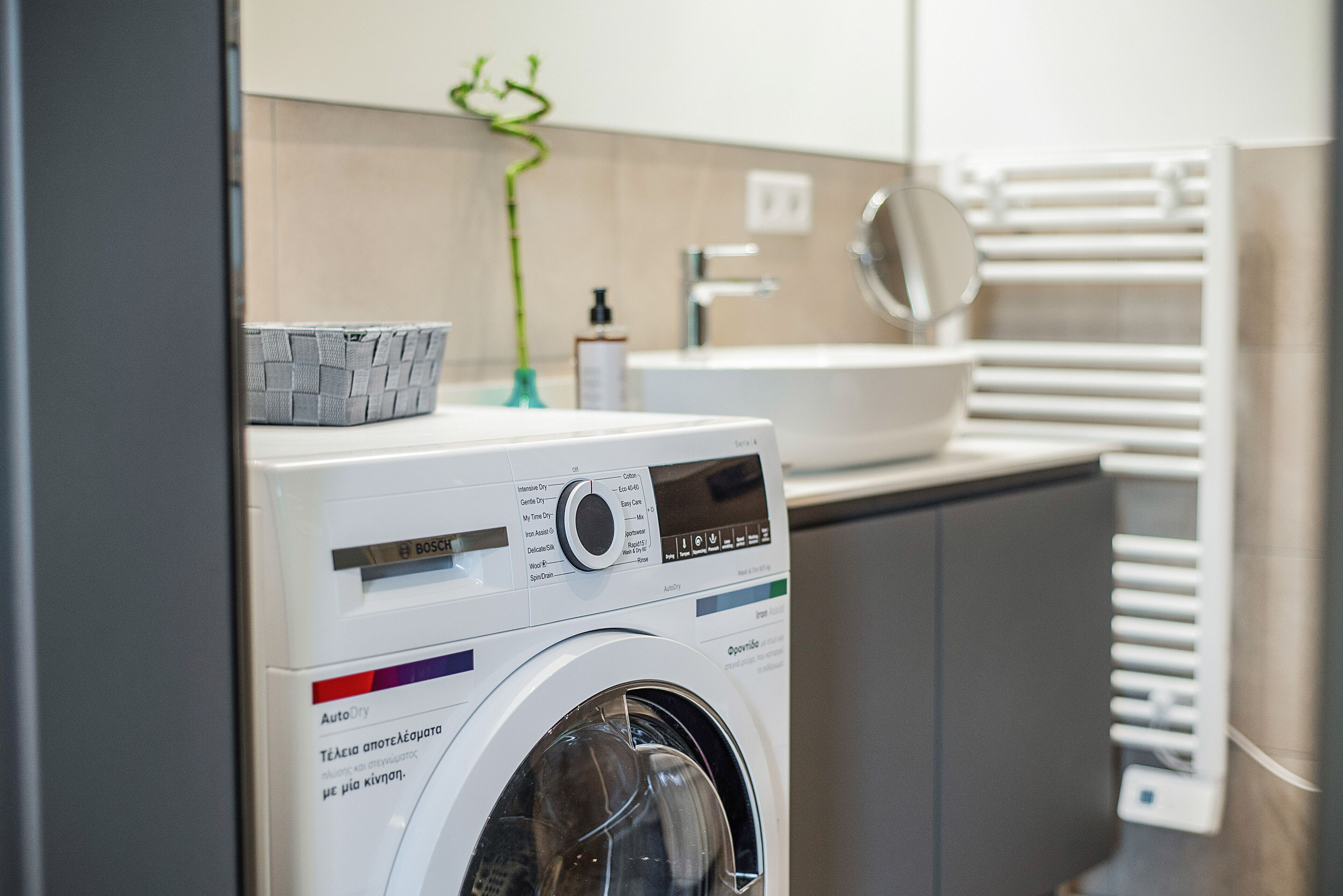 A front-loading washing machine in a modern bathroom with a sink and towel rack.