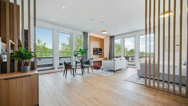 Un salon moderne avec un plancher en bois, un canapé blanc, une table à manger avec des chaises et une grande fenêtre donnant sur un paysage verdoyant.