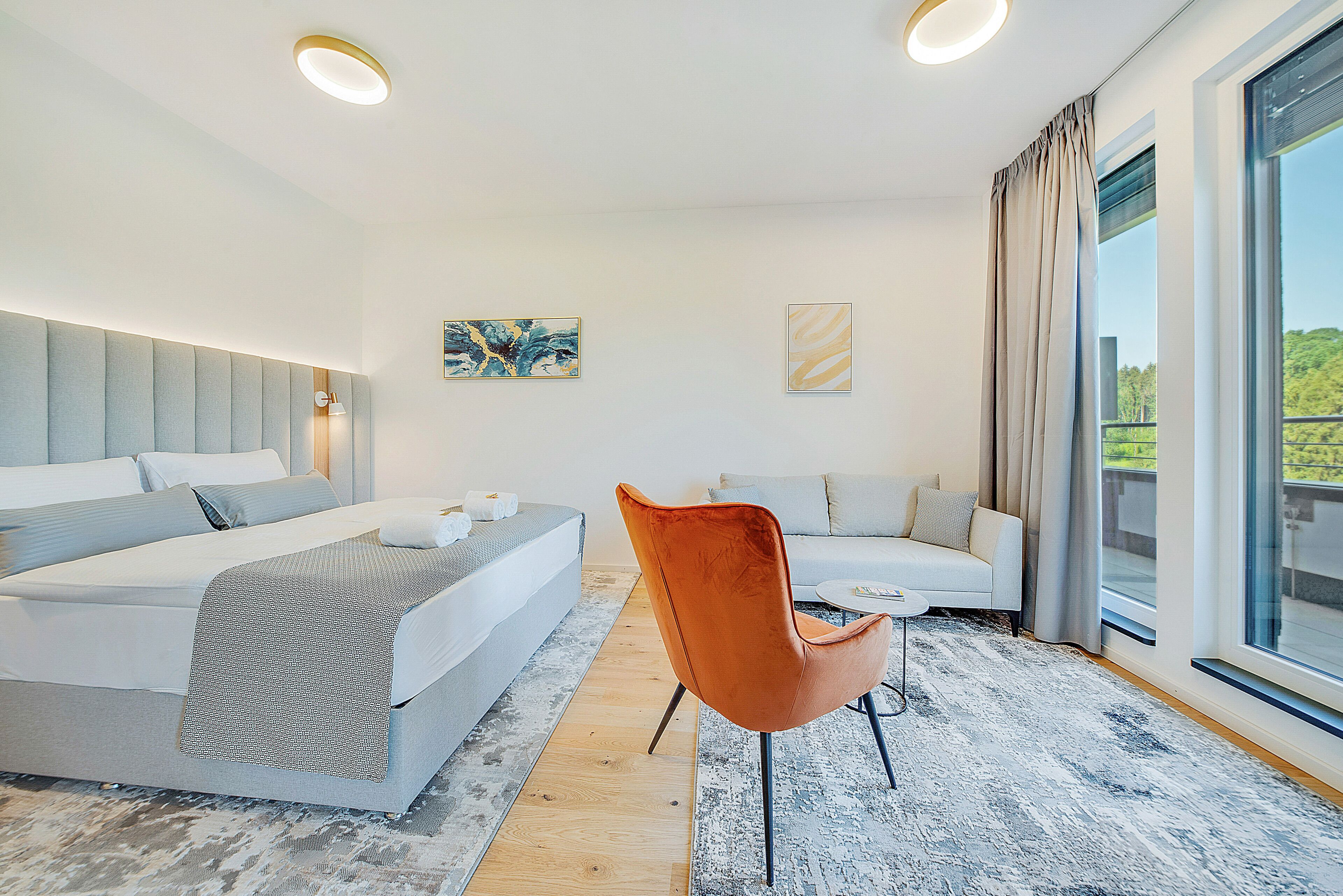 Habitación de hotel moderna con una cama grande, un sofá, una silla y vistas al exterior.