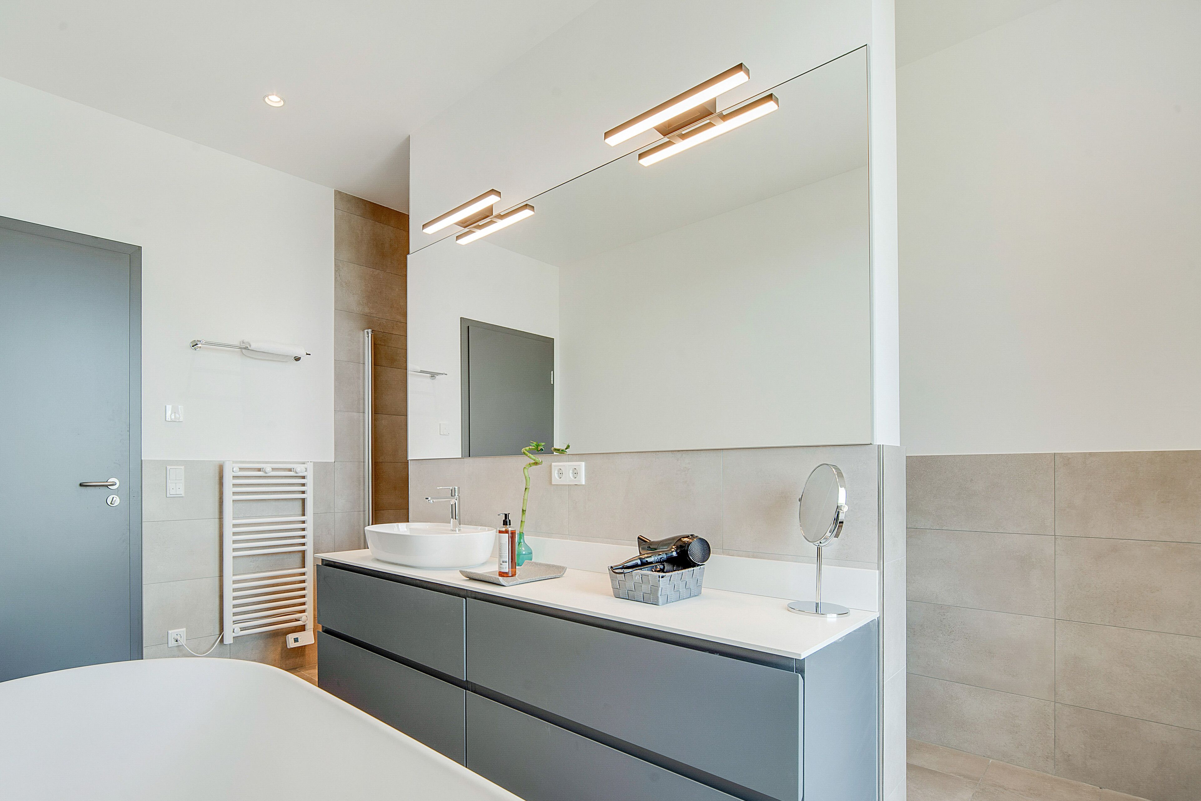 A modern bathroom with a white sink, mirror, and towel rack.