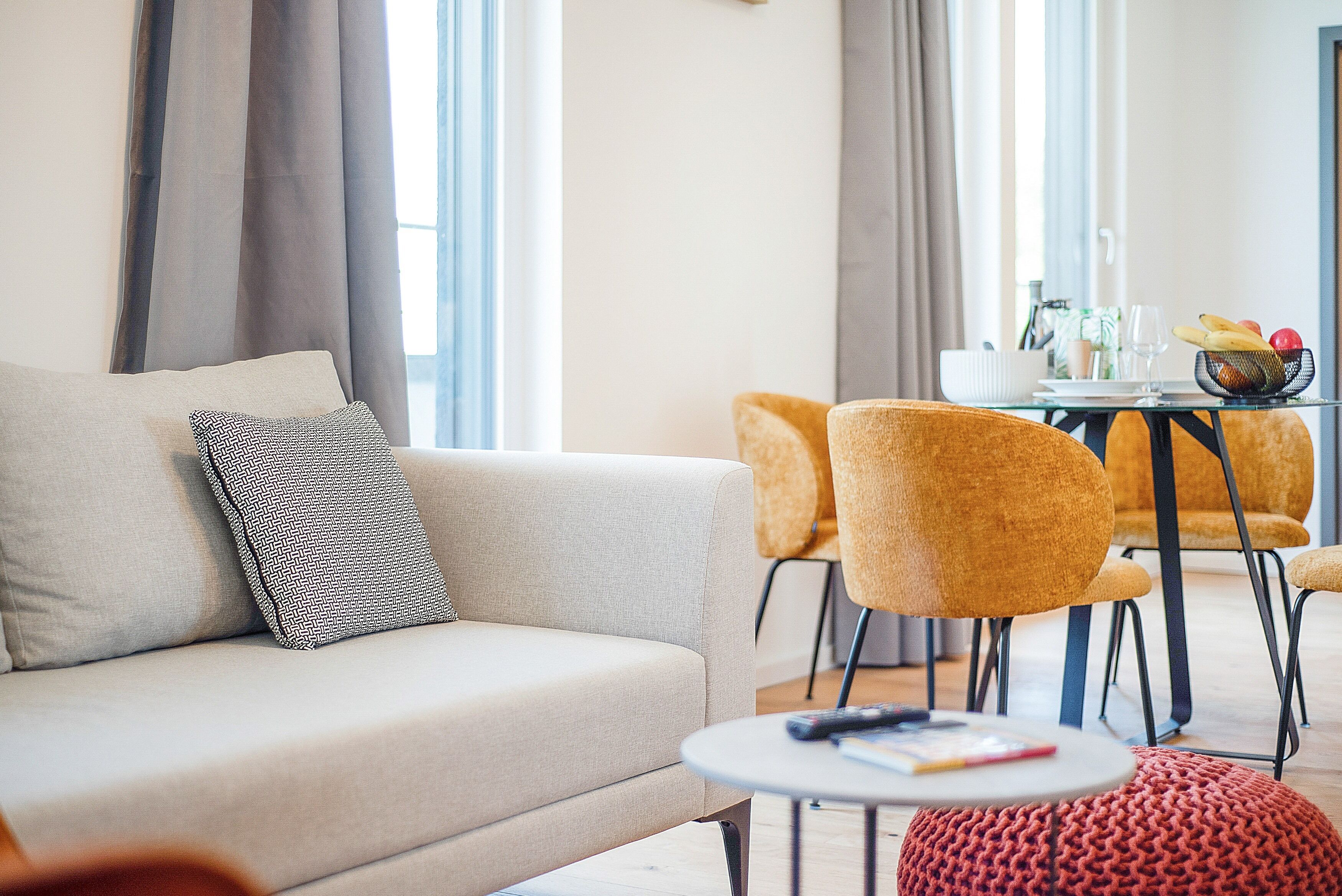 A modern living room with a sofa, a round coffee table, and a dining area with yellow chairs and a glass table.