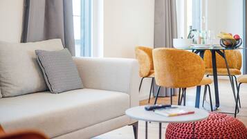 A modern living room with a sofa, a round coffee table, and a dining area with yellow chairs and a glass table.