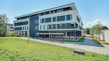 A modern multi-story building with a covered outdoor seating area and a pathway leading to the entrance.
