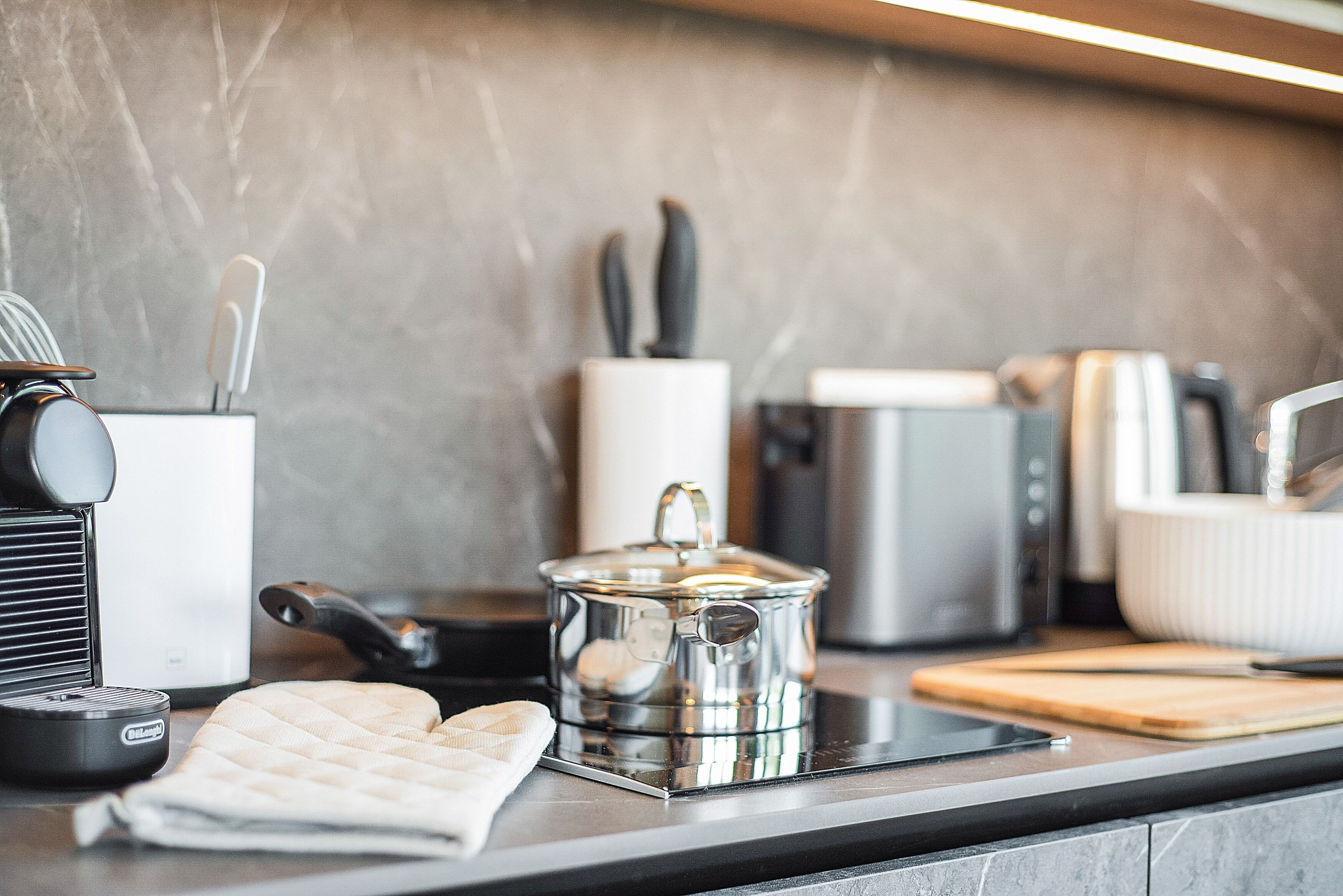 A modern kitchen with a coffee maker, a kettle, a toaster, and a cutting board on the counter.