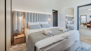Une chambre moderne avec un grand lit, des tables de chevet, une commode, une plante en pot et un miroir.