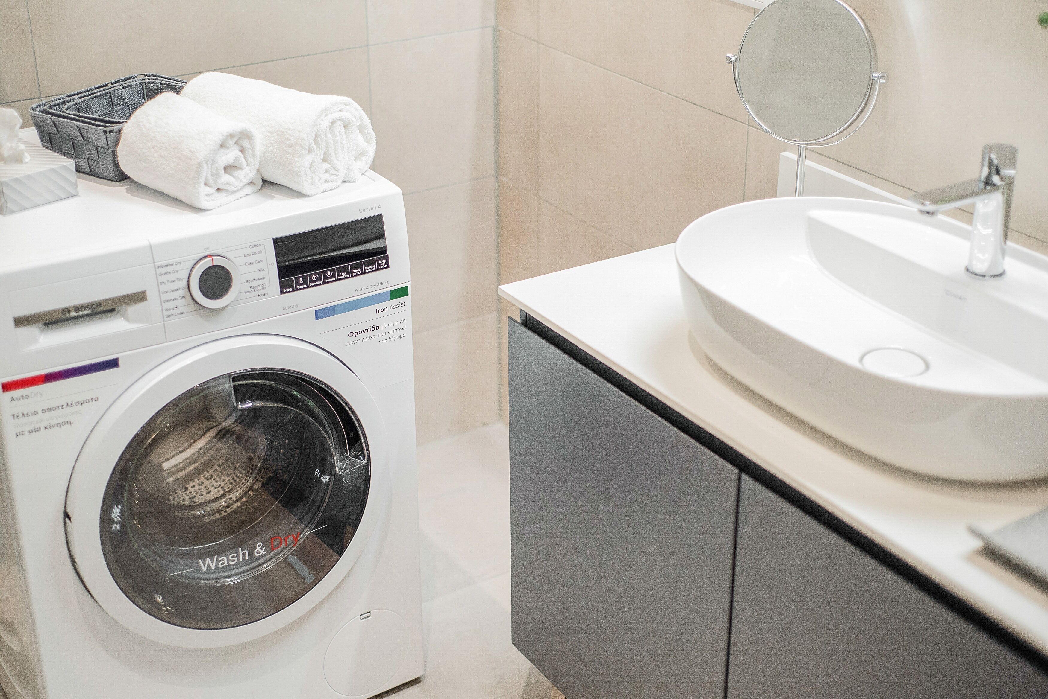Un baño moderno con una lavadora de carga frontal, un lavamanos y un espejo.