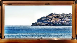 Une vue sur la côte, aperçue à travers une fenêtre, avec une falaise rocheuse surmontée de bâtiments et la mer en premier plan.
