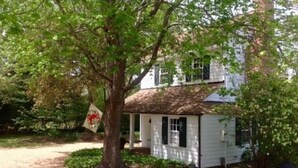 A white house with a porch, surrounded by trees and a gravel path. - Historic Cottage on Ware River Estate (Gloucester)